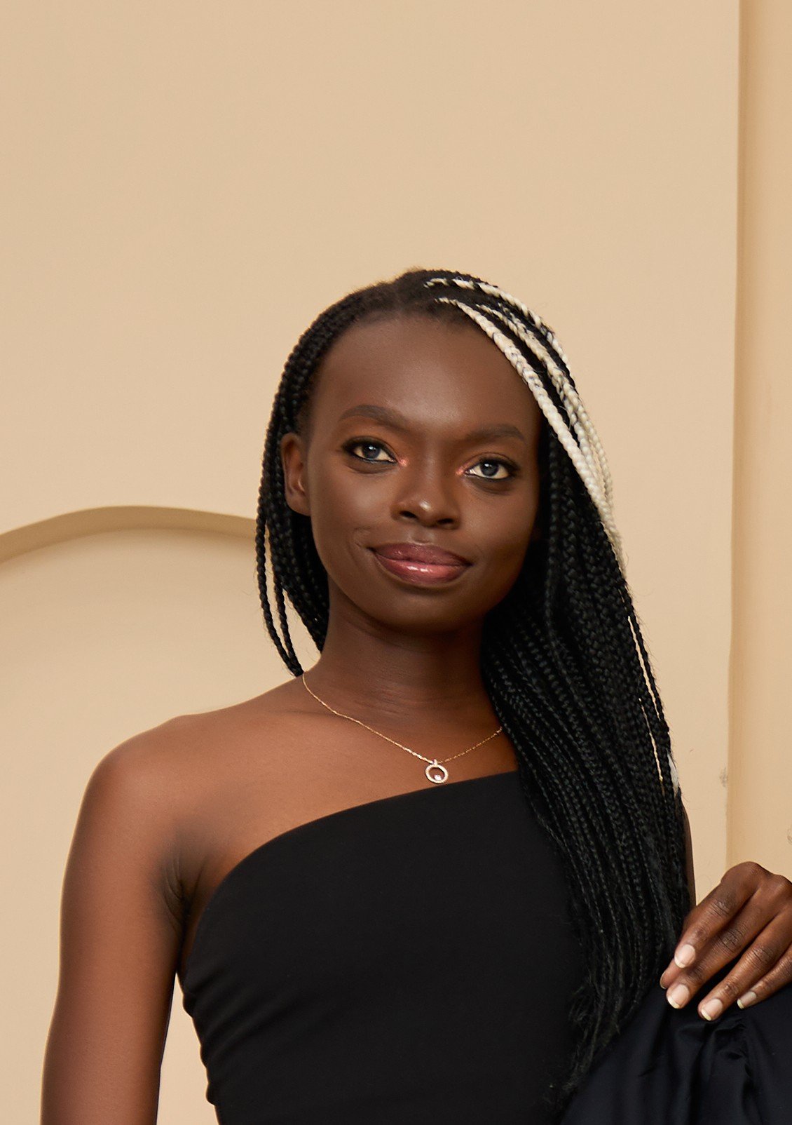 OSANJO in a mustard outfit against a peach backdrop, long braids over one shoulder.