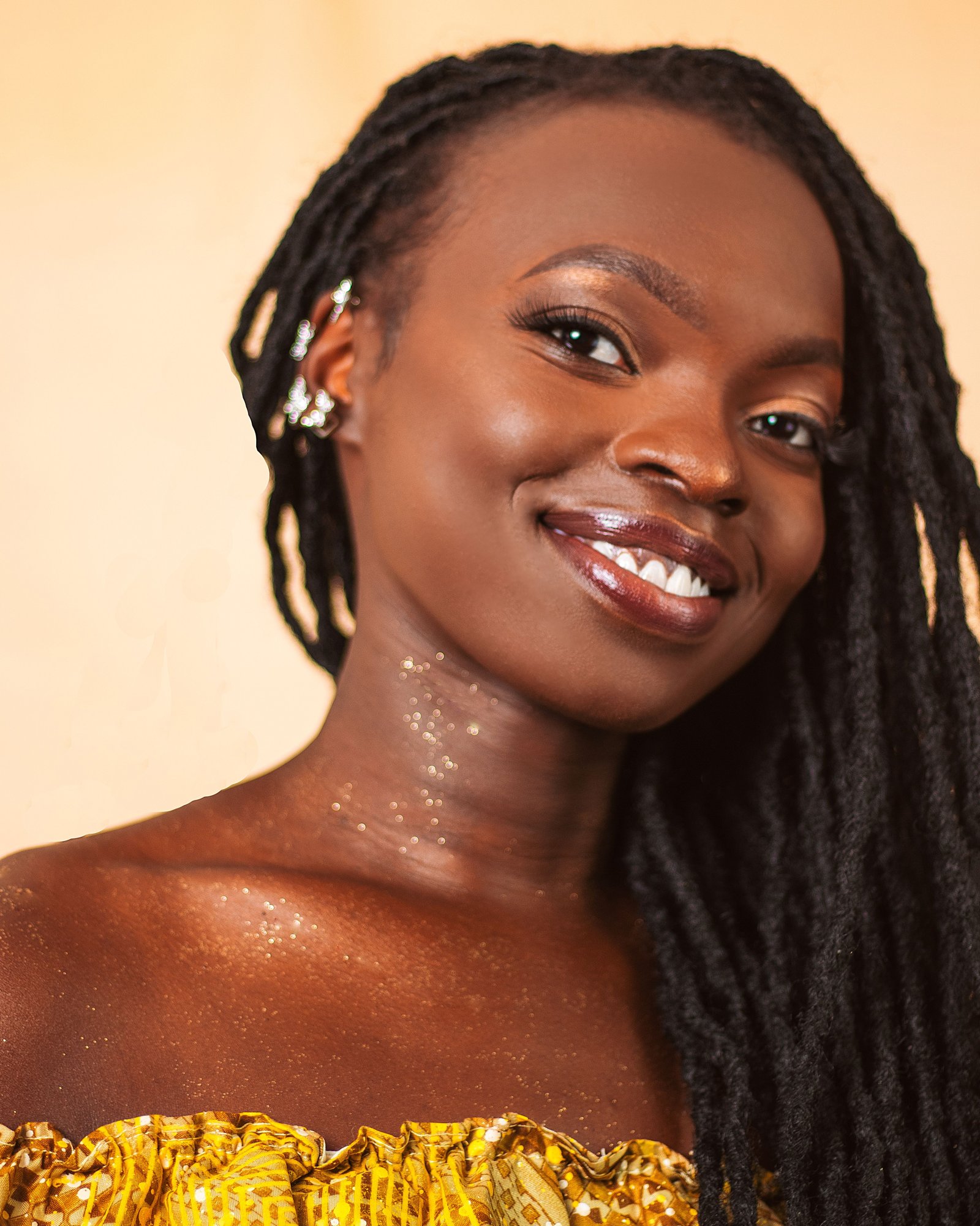 OSANJO in mustard and yellow, long braids, photographed against a warm peach backdrop.