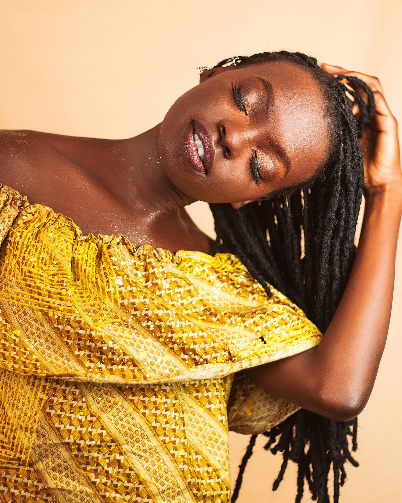A third portrait of OSANJO in a mustard outfit, peach light behind her.