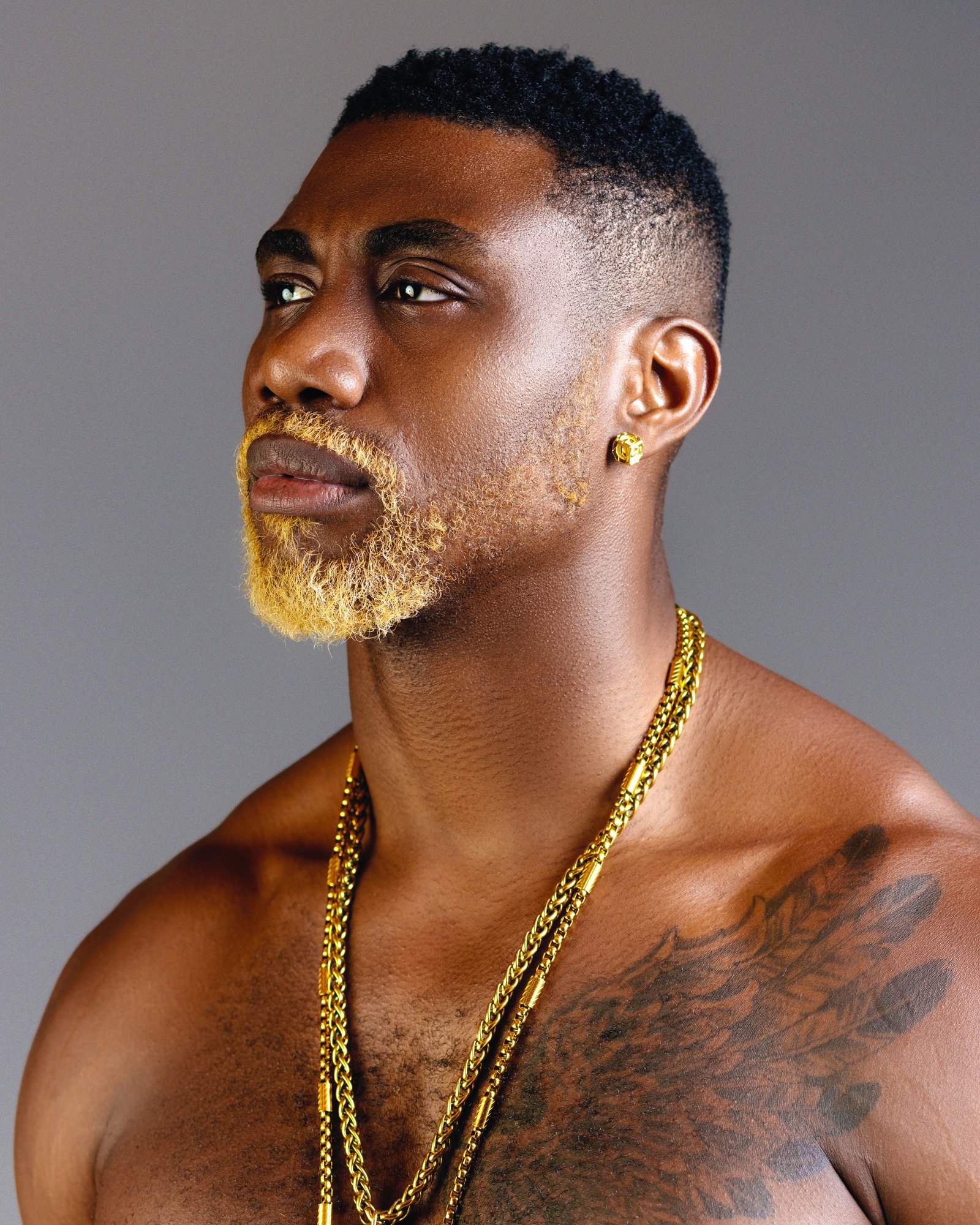 6UFF in the studio, shirtless, wearing gold chains against a grey backdrop.