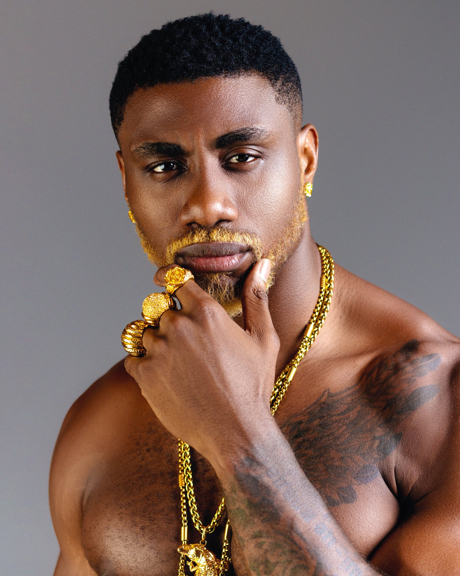 A second studio portrait of 6UFF, shirtless, in gold chains against a grey backdrop.